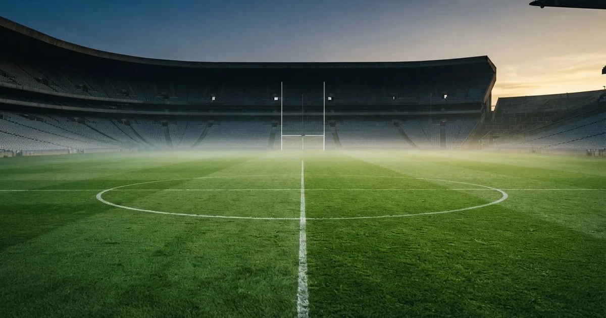 Ein Fußballplatz mit gepflegtem Rasen und einem Tor, über dem Spielfeld liegt Morgennebel, im Hintergrund eine leere Tribüne.