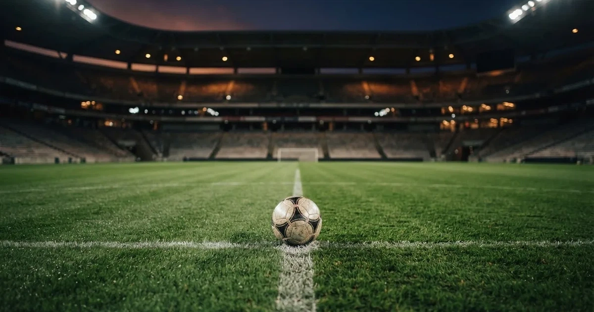 Ein Fußball liegt auf dem Rasen eines leeren Stadions bei Flutlicht, im Hintergrund unscharfe Tribünen ohne erkennbare Beschriftung.