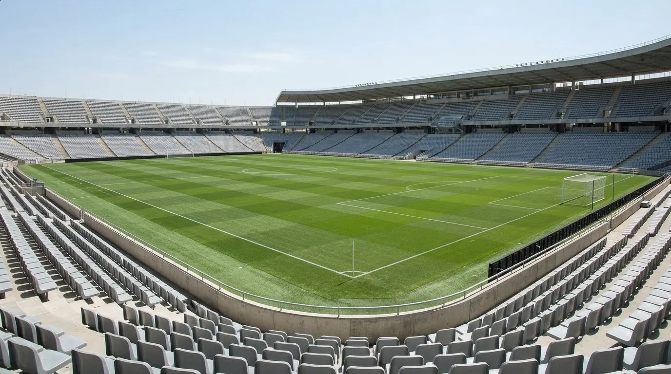 Ein leeres Fußballstadion bei Tageslicht von der Tribüne aus gesehen, der Rasen zeigt gleichmäßige Mähstreifen.