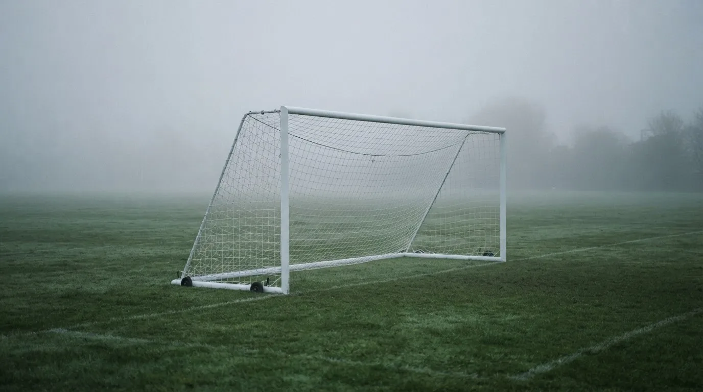Ein Fußballtor mit Netz im Morgennebel auf einem leeren Platz, die Linien nur schwach zu erkennen.