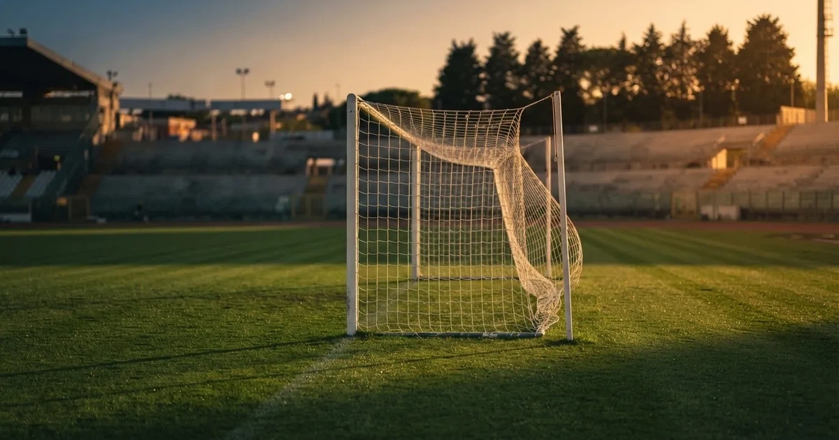 Ein Fußballtor mit Netz auf einem leeren Platz im Abendlicht, der Rasen frisch gemäht, im Hintergrund Zypressen.