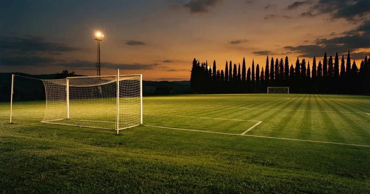 Ein Fußballtor mit Netz auf einem leeren Platz im Abendlicht, der Rasen frisch gemäht, im Hintergrund Zypressen.