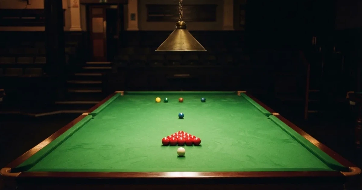 Ein Snookertisch mit grünem Tuch und aufgebauten roten Kugeln in einem abgedunkelten Raum unter einer hängenden Lampe.